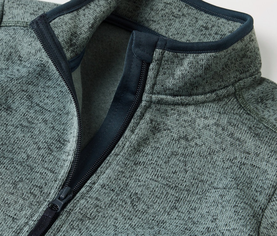 Détail d'une veste en maille polaire hybride pour enfant avec fermeture éclair ouverte.