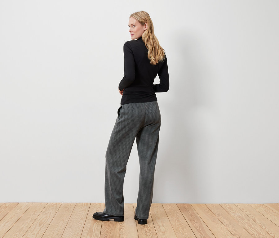 Blonde portant un haut noir et un pantalon gris regardant par-dessus son épaule.