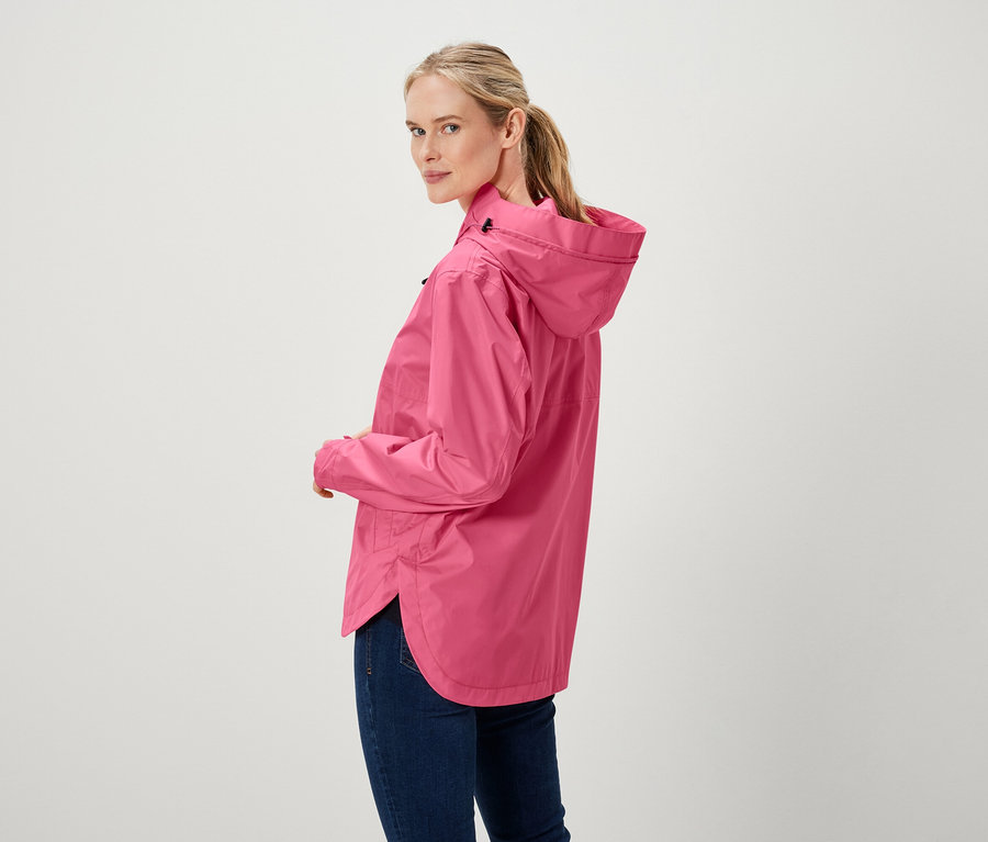 Une femme regarde par-dessus son épaule et porte une veste rose et un jean.