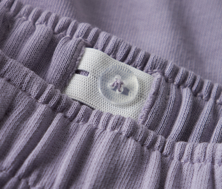 Gros plan de la ceinture d'un pantalon violet avec élastique réglable et bouton.