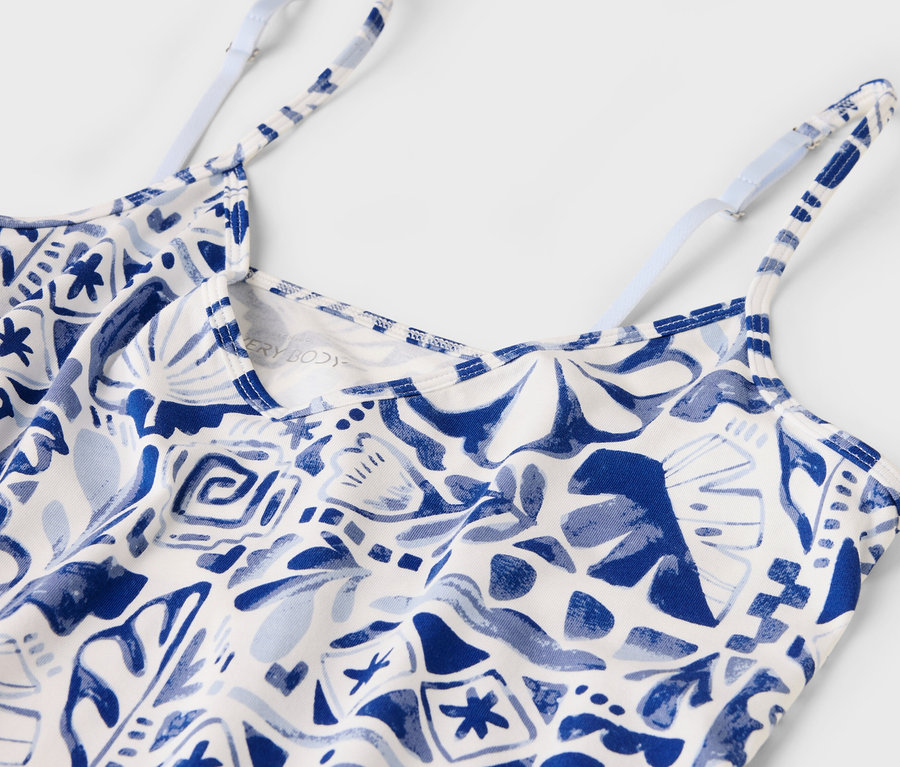 Gros plan d'un débardeur blanc à motifs bleus avec de fines bretelles réglables.