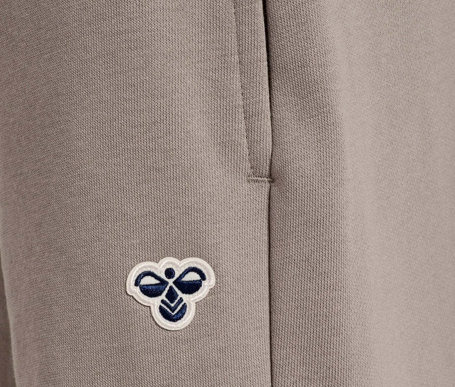 Gros plan d'un pantalon de jogging beige avec un patch d'abeille Hummel cousu.
