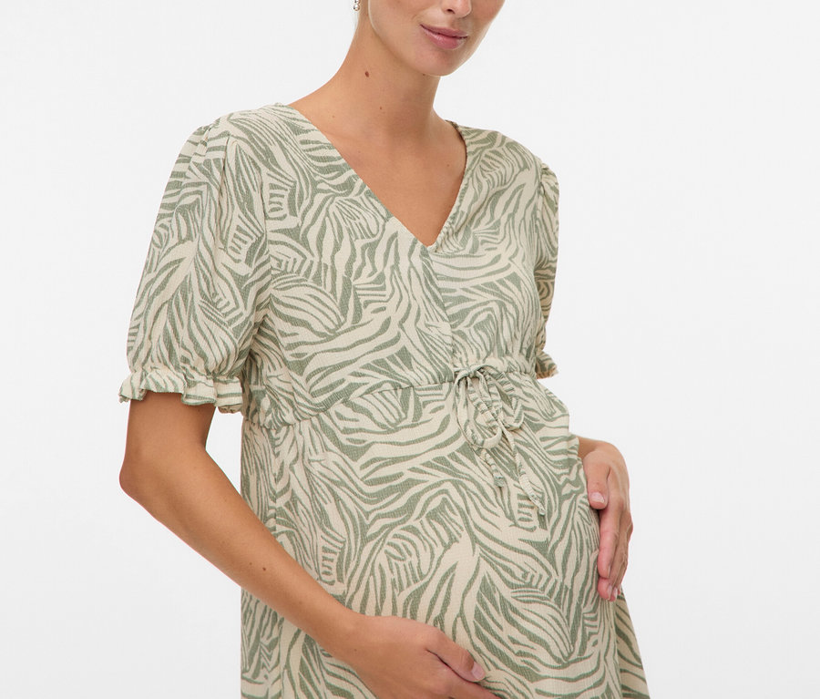 Femme enceinte portant une robe à motifs, les mains sur le ventre.