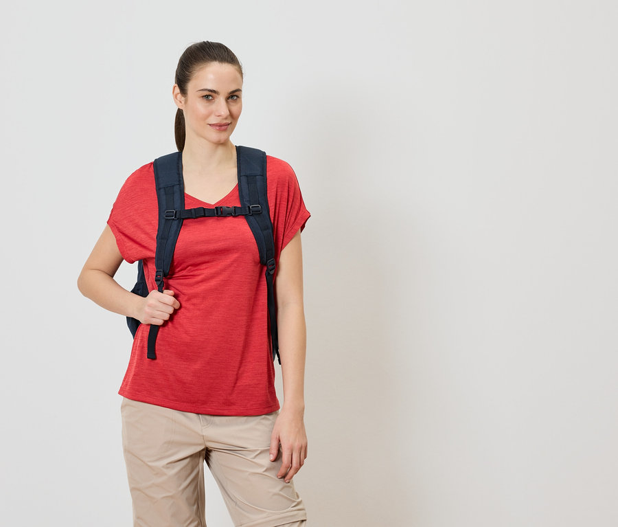 Femme portant un sac à dos bleu marine sur un t-shirt rouge et un pantalon beige.