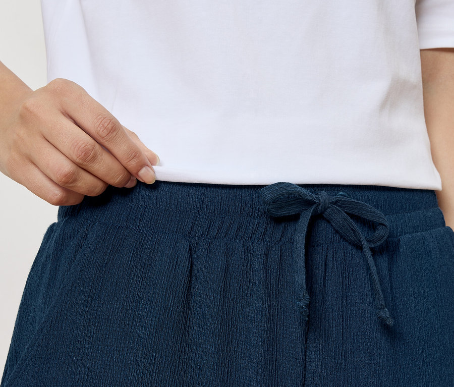 Gros plan d'une personne portant un t-shirt blanc et un pantalon bleu marine avec cordon de serrage.