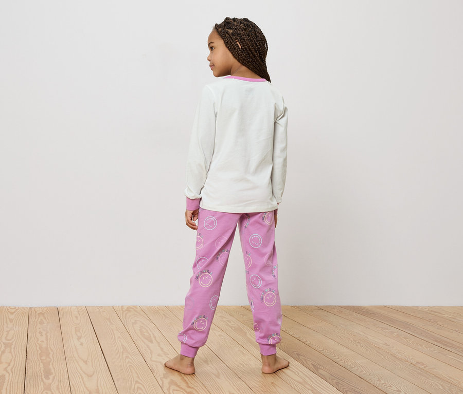 Vue de dos, une fillette avec des tresses porte un haut blanc et un pantalon rose avec des smileys.