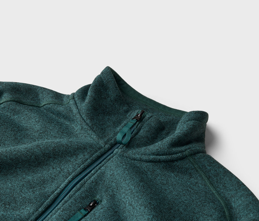Gros plan d'une veste polaire verte avec fermeture éclair et col montant sur fond neutre.