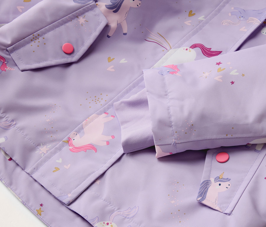 Gros plan d'une veste violette à motif de licorne, d'une poche avec un bouton rose et d'une manche.
