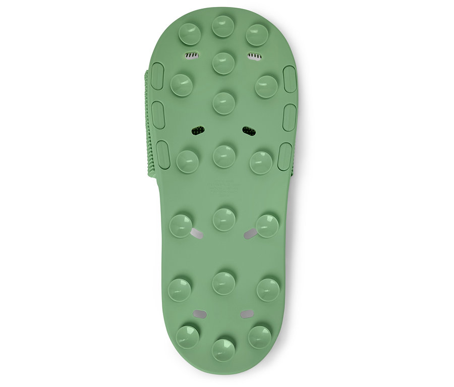 Gros plan d'une seule sandale de bain verte avec des picots sur un fond blanc.