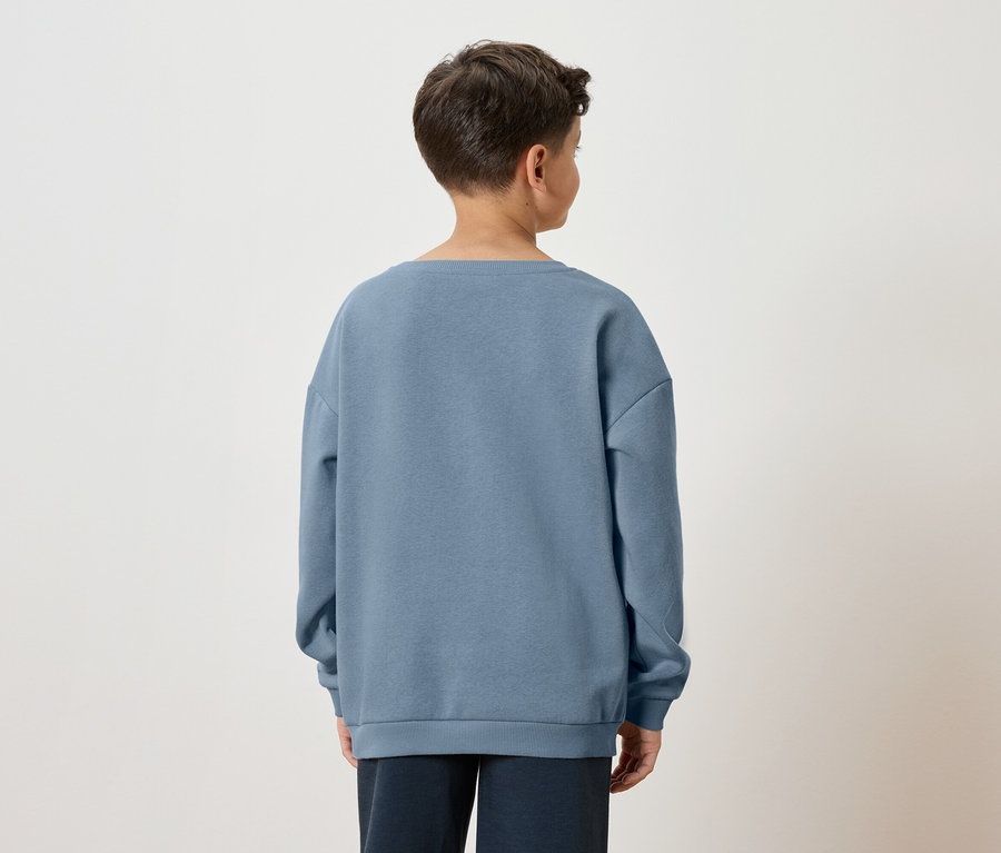 Vue arrière d'un garçon aux cheveux bruns portant un pull bleu et un pantalon foncé sur un fond blanc.