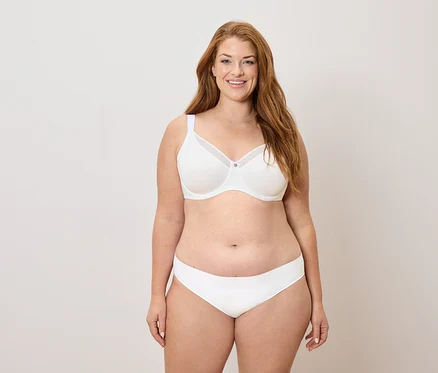 Femme aux longs cheveux roux portant un soutien-gorge et une culotte blancs, souriant.
