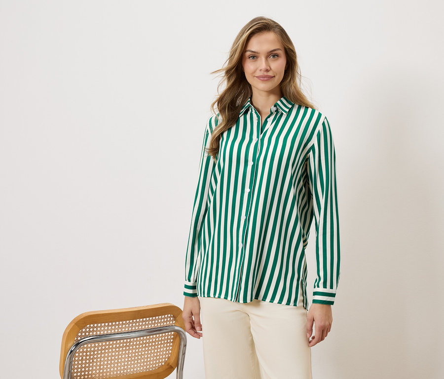 Femme portant une chemise à rayures vertes et blanches et un pantalon beige, à côté d'une chaise.