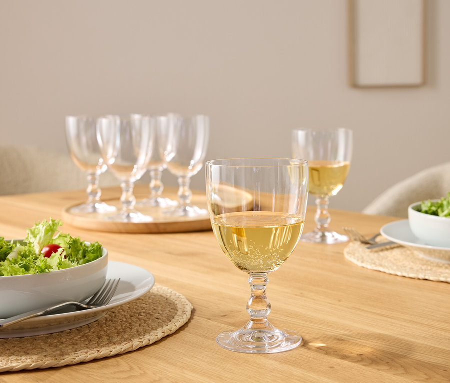 Sur une table en bois, des saladiers et des verres à vin, dont certains sont remplis de vin blanc.