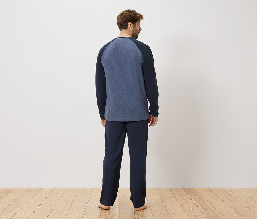 Un homme se tient dos à la caméra, vêtu d'un pyjama bleu marine.
