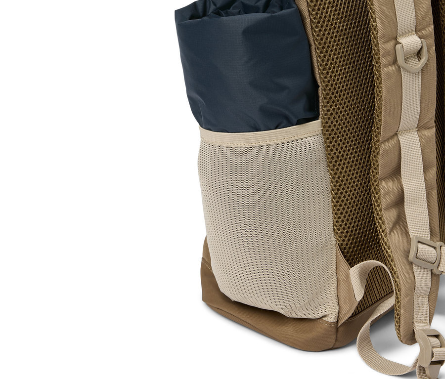 Gros plan d'un sac à dos beige avec un rouleau de tissu bleu foncé dans une poche latérale en filet.