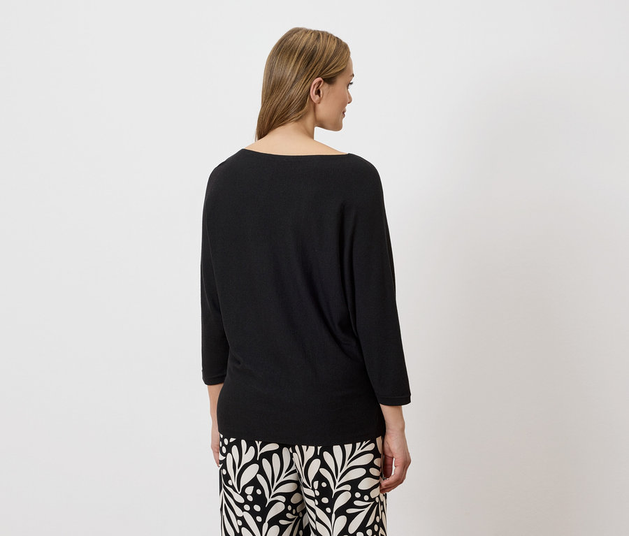 Vue arrière d'une femme aux cheveux blonds portant un pull noir et un pantalon à motifs.