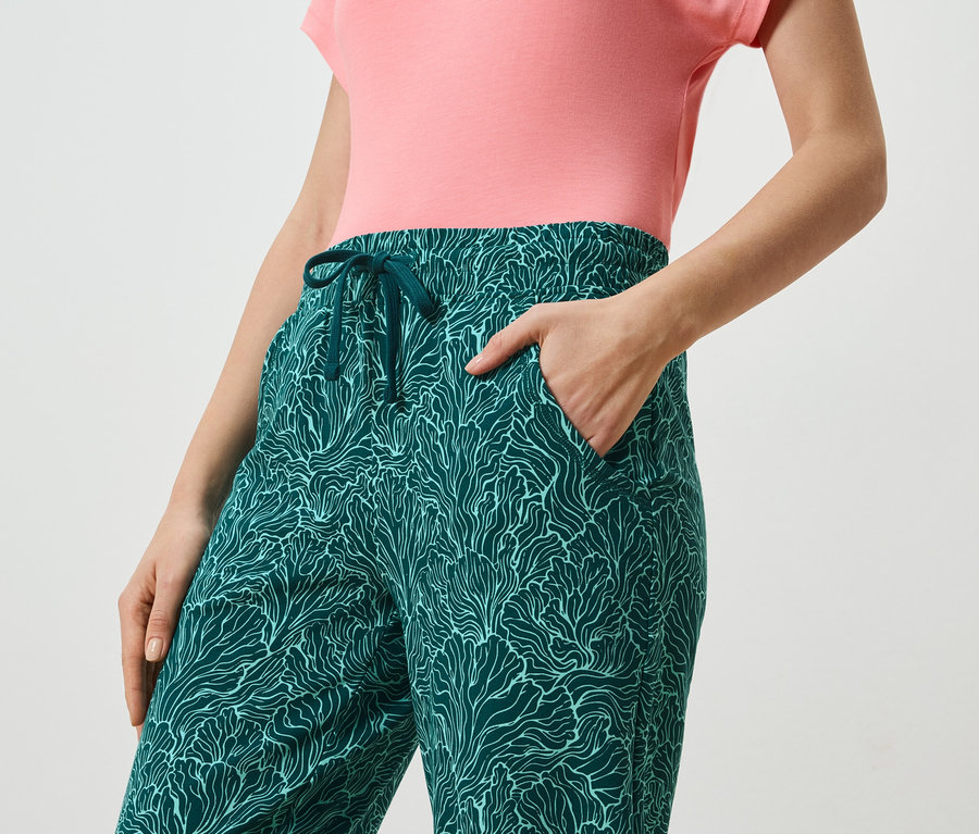 Une femme porte un chemisier corail et un pantalon pétrole à motif abstrait avec cordon de serrage.