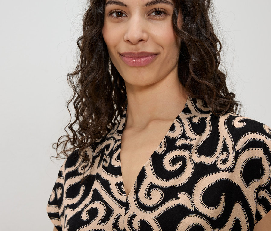 Portrait d'une femme aux cheveux bouclés portant un haut à motifs noirs et beiges.