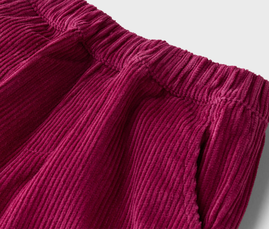 Gros plan d'un pantalon en velours côtelé bordeaux avec une taille élastique et une poche.