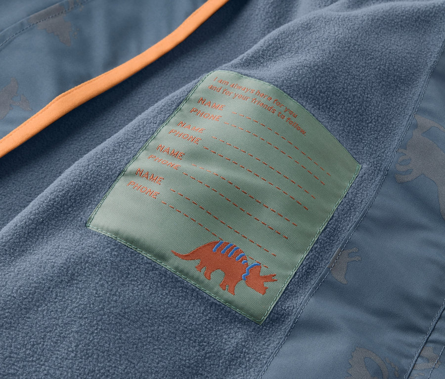 Gros plan sur l'intérieur d'une veste bleue avec une bordure orange et une étiquette avec un dinosaure et un espace pour le nom et le numéro de téléphone.