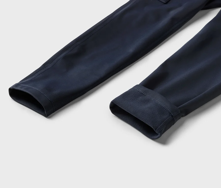 Deux manches bleu foncé d'un vêtement, l'une à plat montrant le tissu extérieur et l'autre retroussée pour révéler une doublure douce de type polaire, sur un fond gris clair.