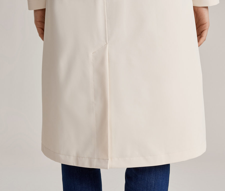 Vue arrière d'une personne portant un jean et un long manteau crème.
