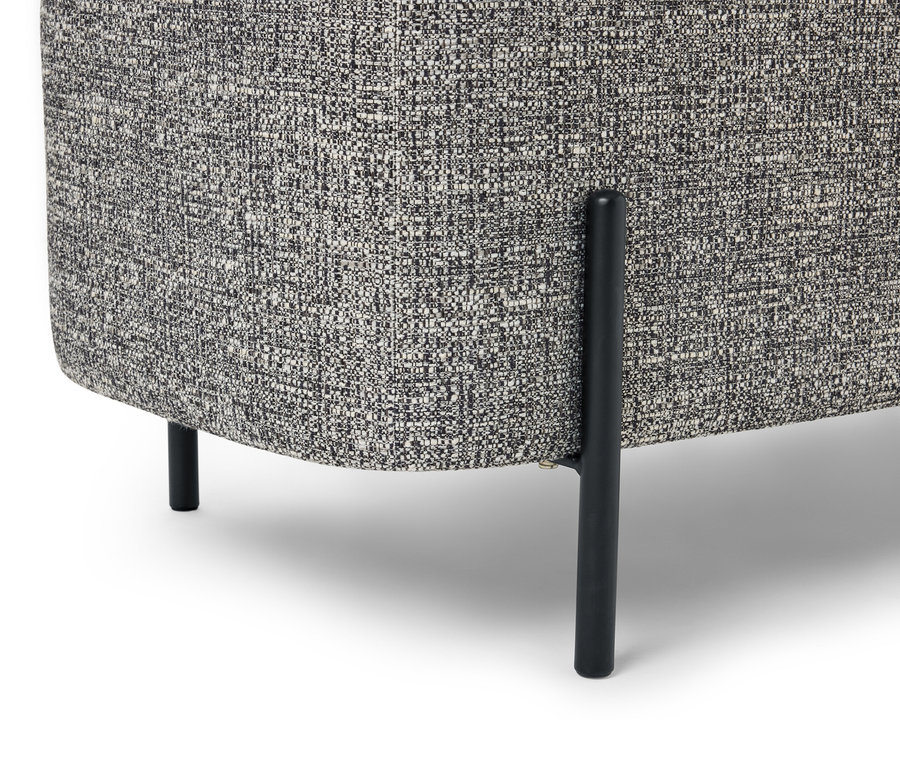 Gros plan sur le coin d'un fauteuil avec un tissu chiné gris et des pieds noirs sur fond blanc.