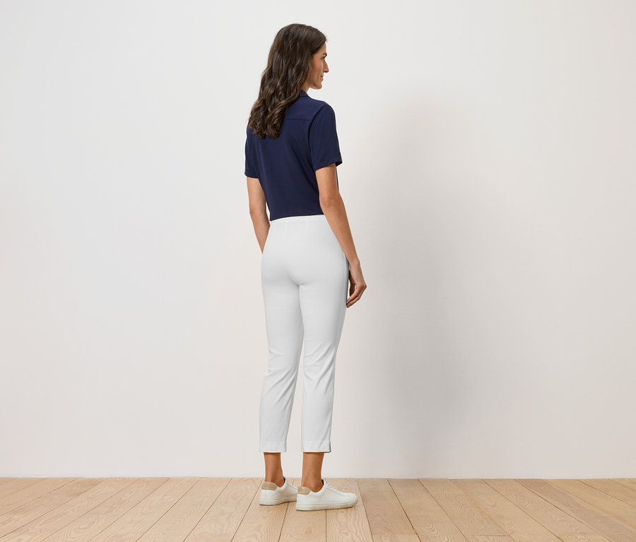 Une femme se tient dos à la caméra, elle porte un polo bleu marine, un pantalon blanc et des chaussures blanches.