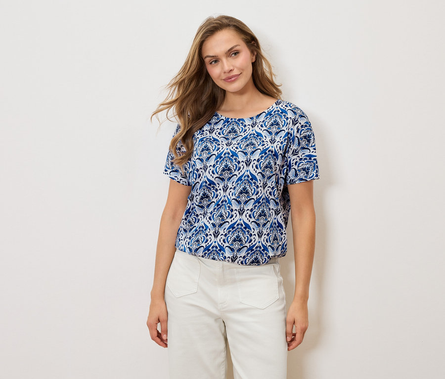 Une femme porte un t-shirt à motifs bleus et blancs et un pantalon blanc sur un fond blanc.