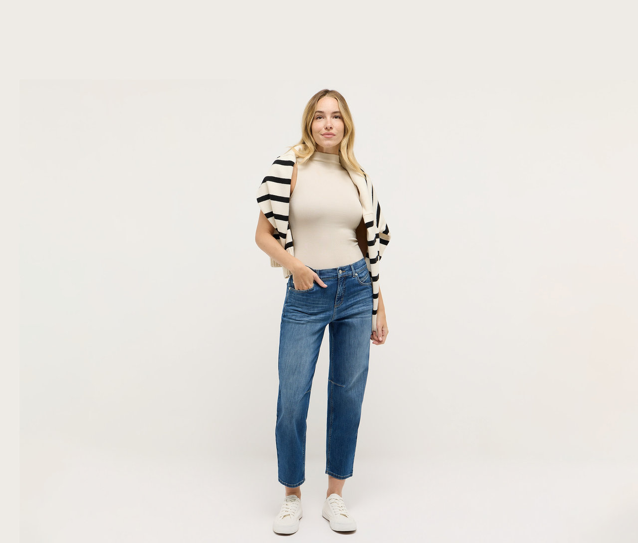 Femme portant un jean Angels Denim « Evi », un haut beige et un cardigan rayé noir et blanc.