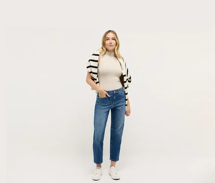 Femme portant un jean Angels Denim « Evi », un haut beige et un cardigan rayé noir et blanc.