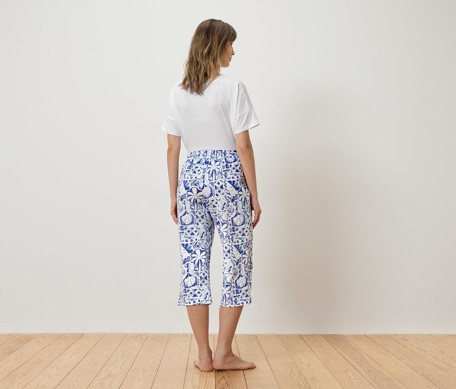 Femme vue de dos portant un t-shirt blanc et un pantacourt bleu à motifs.