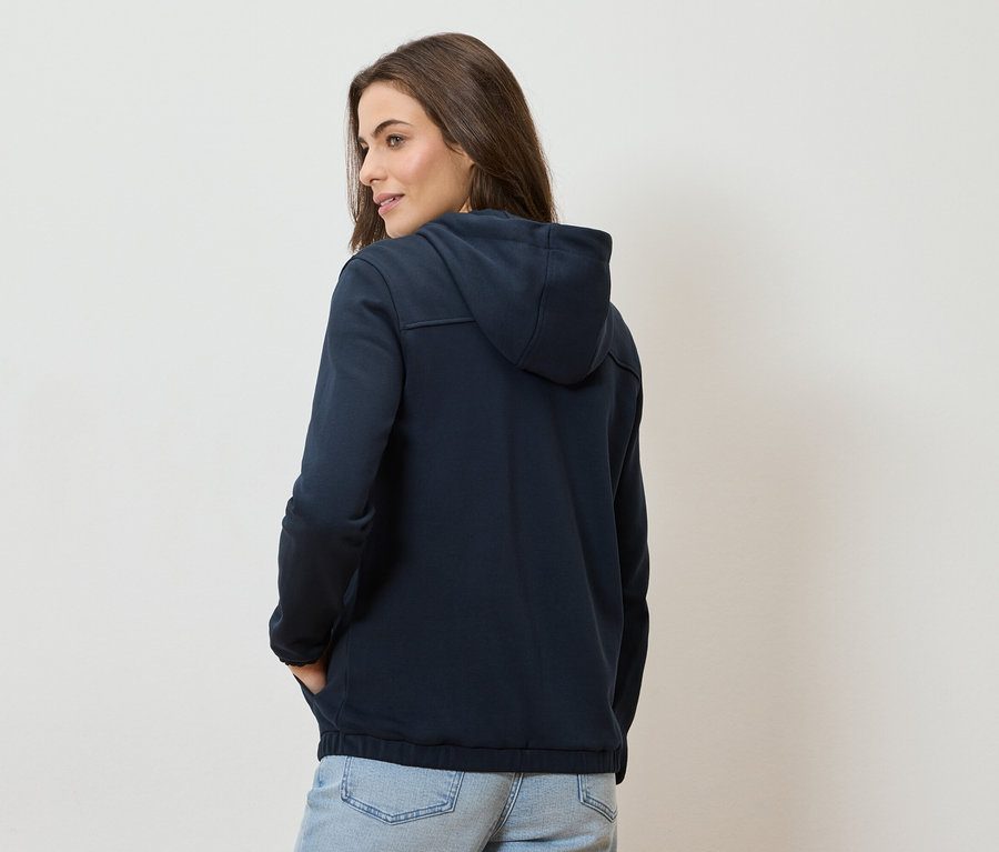 Une femme porte un sweat à capuche bleu marine et un jean bleu clair.
