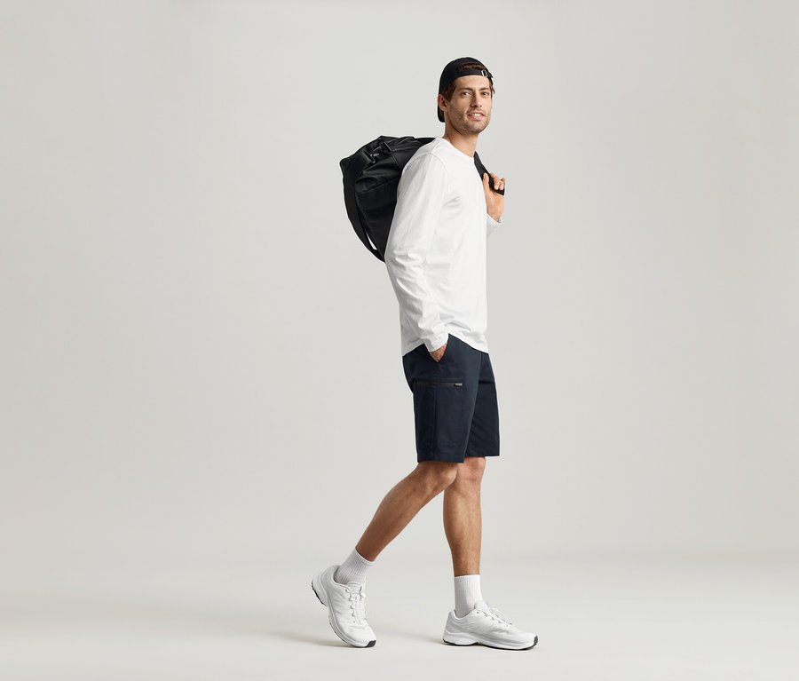 Un homme marche avec un sac noir sur l'épaule et porte 2 T-shirts manches longues.