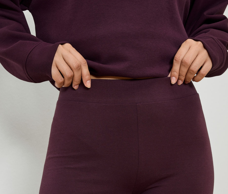 Gros plan d'une personne portant un haut et un legging bordeaux, tenant la taille du legging.