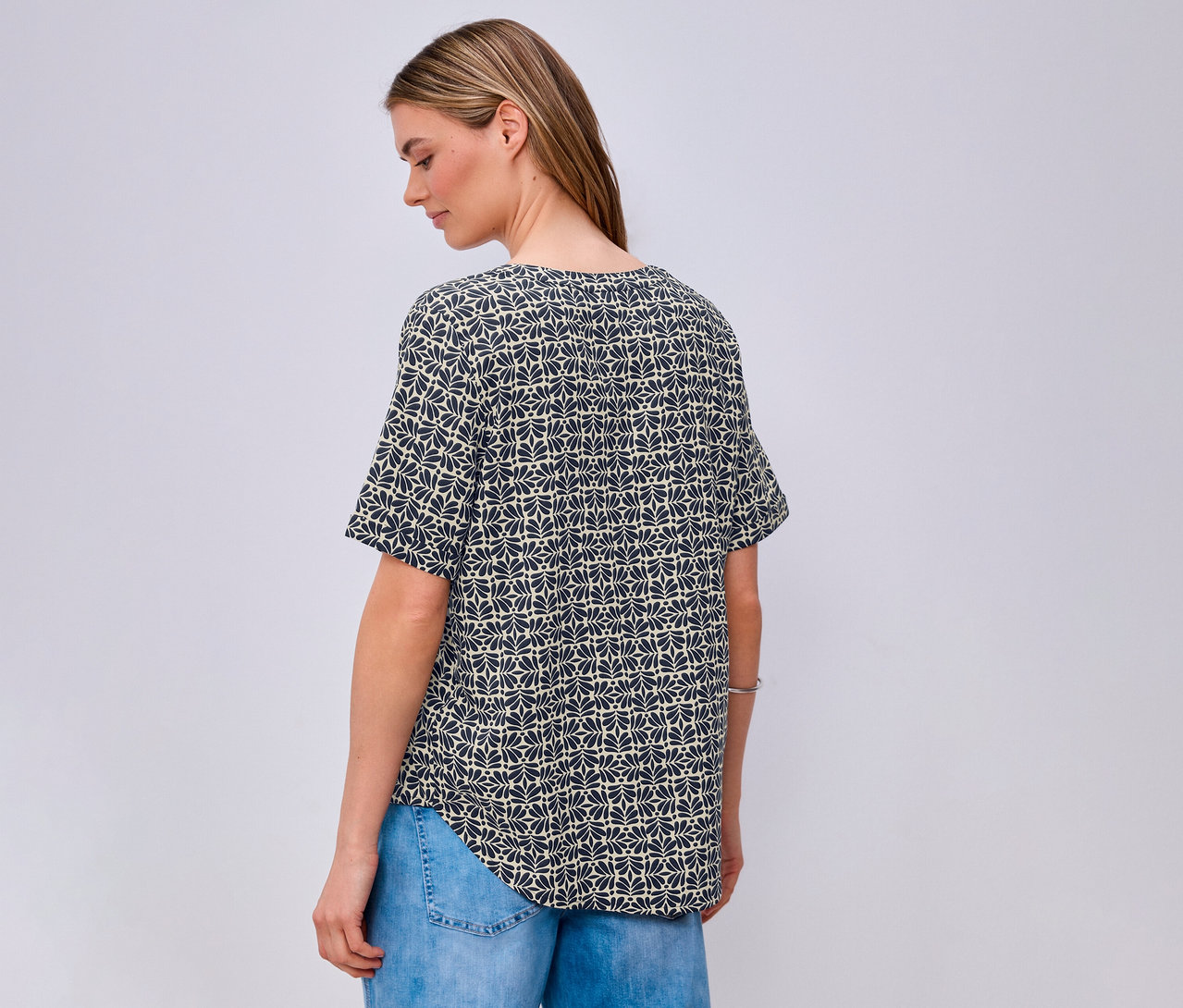 Femme vue de dos portant une blouse en maille Street One à motif bleu et un jean.