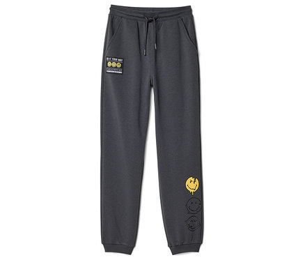 Pantalon de jogging pour enfant SMILEYWORLD® gris foncé avec cordon de serrage, un patch "DO IT YOUR WAY" et trois visages souriants fondus sur la jambe droite.
