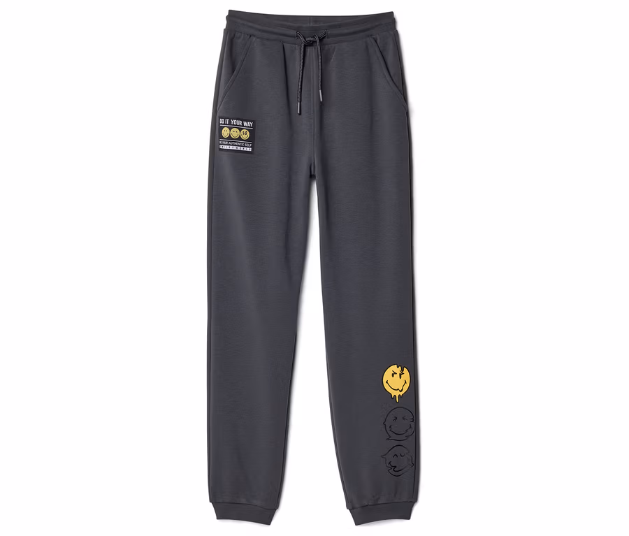 Pantalon de jogging pour enfant SMILEYWORLD® gris foncé avec cordon de serrage, un patch "DO IT YOUR WAY" et trois visages souriants fondus sur la jambe droite.