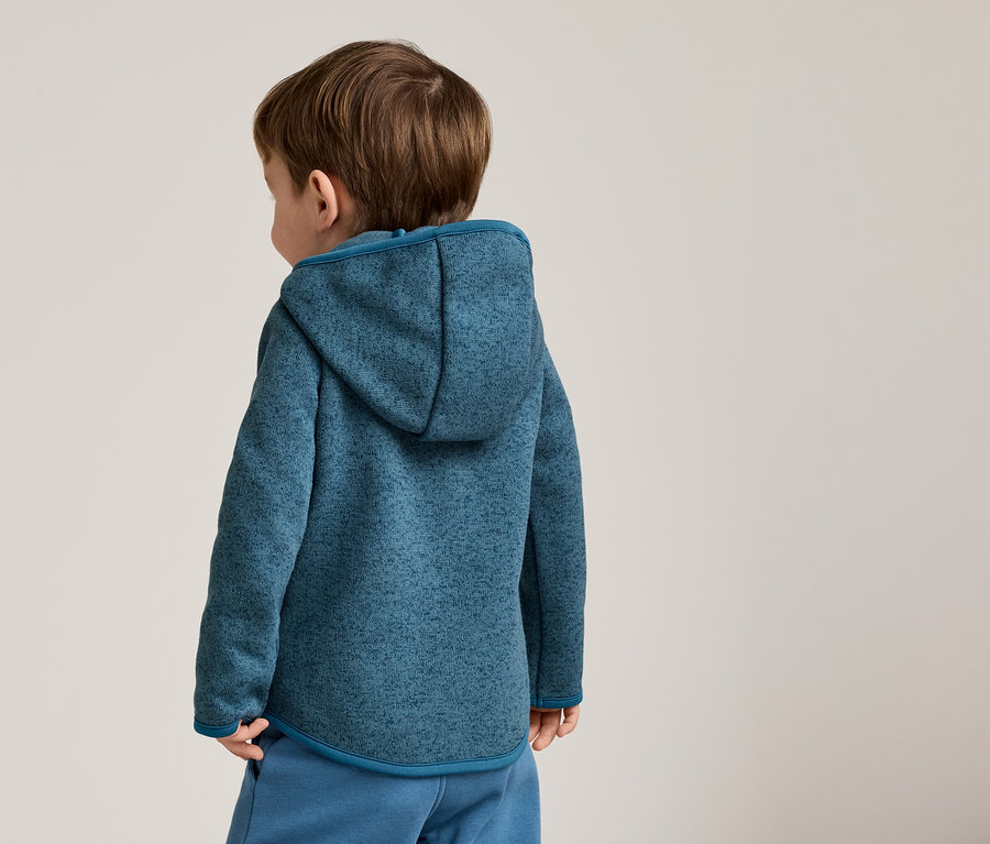 Vue arrière d'un enfant aux cheveux bruns portant un sweat à capuche chiné bleu et un pantalon bleu.