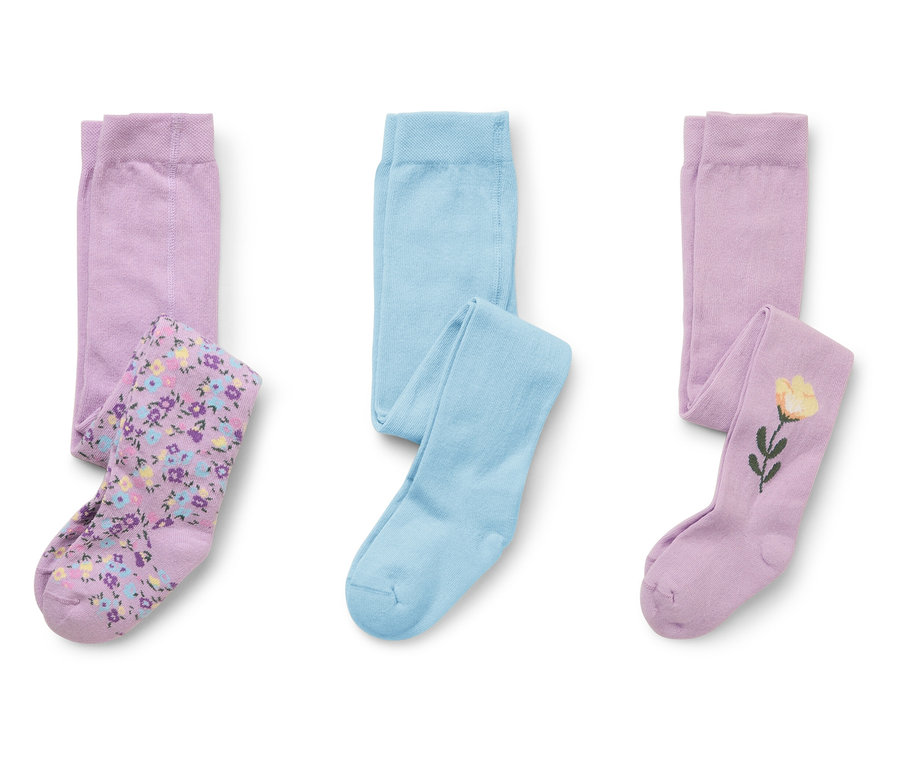 Trois paires de collants pour enfants sont posées sur un fond blanc. Une paire est bleu clair, une paire est violette avec un motif floral et une paire est violette avec une fleur jaune.
