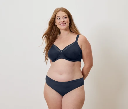 Femme aux longs cheveux roux portant un soutien-gorge et une culotte bleu marine, souriant.
