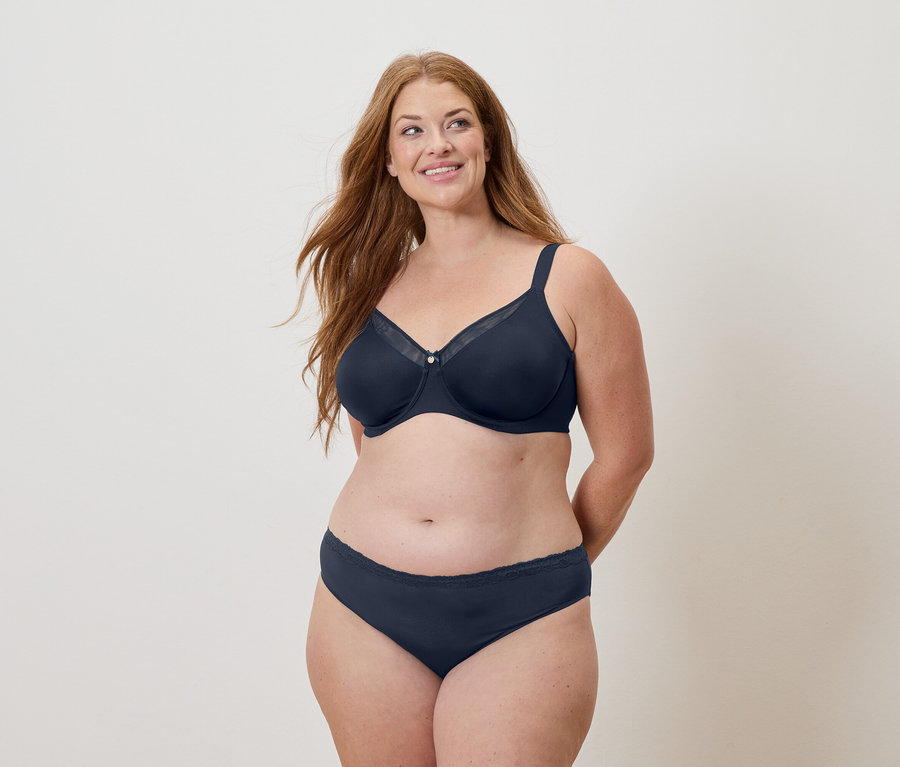 Femme aux longs cheveux roux portant un soutien-gorge et une culotte bleu marine, souriant.