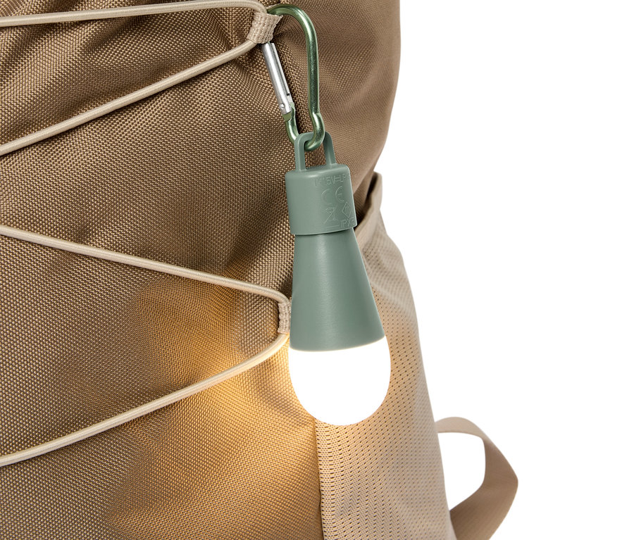 Gros plan d'une lampe LED vert olive fixée à un sac à dos beige par un mousqueton.