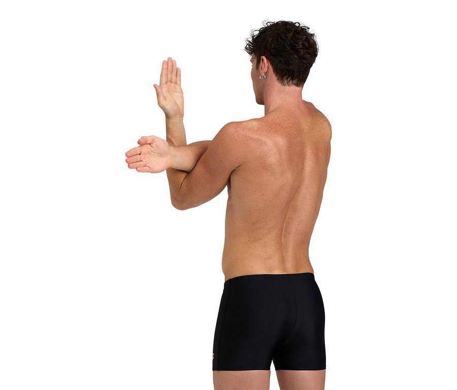 Homme étire ses bras, porte un short de bain noir.