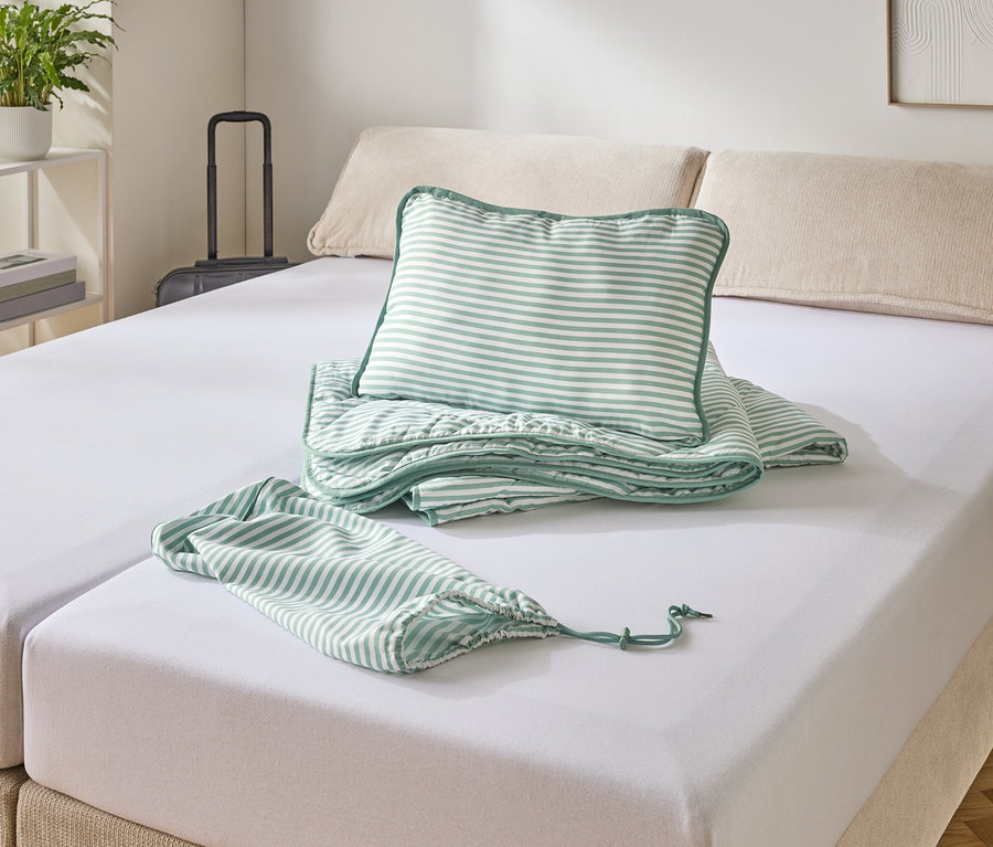 Un lit avec un drap-housse blanc, sur lequel reposent un oreiller rayé, une couverture et un sac.