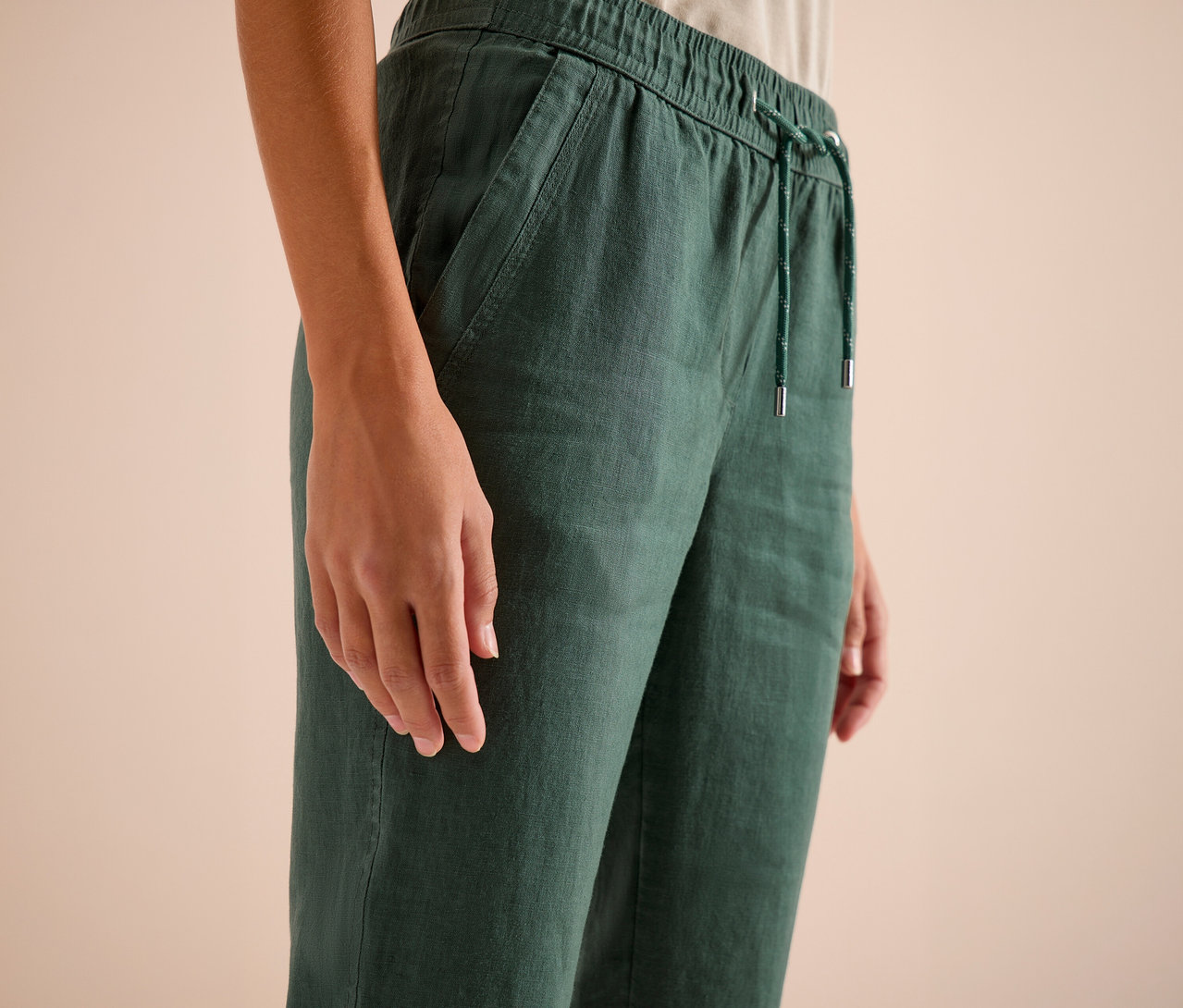 Gros plan d'une personne portant un pantalon en lin vert avec cordon de serrage.