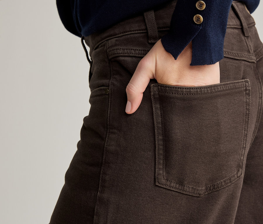 Gros plan d'une personne avec une main dans la poche arrière d'un pantalon marron et un pull bleu marine.
