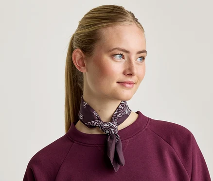Une femme blonde porte un sweat-shirt bordeaux et un foulard à motifs.