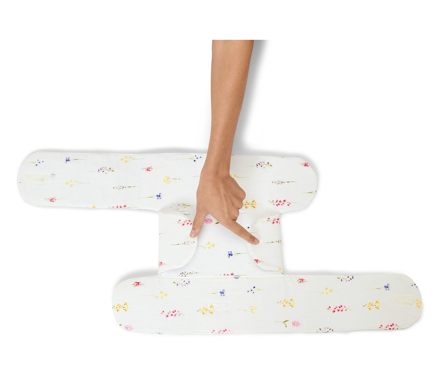 Une main touche un coussin de positionnement blanc à motifs floraux.