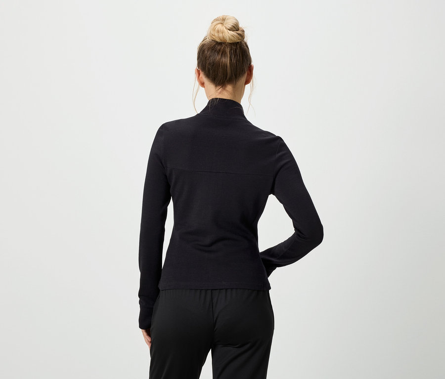 Vue de dos d'une femme portant un chignon, un haut noir à manches longues et un pantalon noir.
